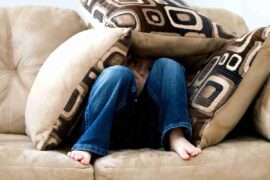 A child crouched under cushions on a couch, conveying a sense of playfulness or fear.