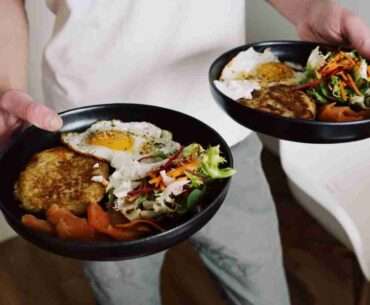 Faceless male in white clothes holding black plates with fried eggs and fresh salad for breakfast in cozy kitchen