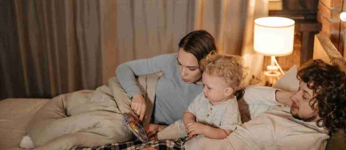 Father and mother reading to their child in bed during nighttime for a cozy bedtime story.