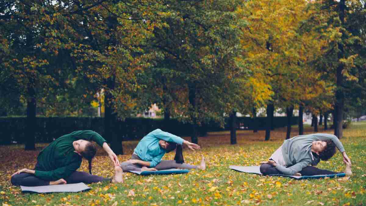Crossfit zu Yoga: Eine streikende Fußsohle und eine neue Routine Three people practicing yoga in a park during fall surrounded by trees.