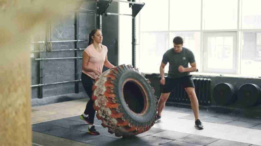 Sport statt Spielplatz - ein Hoch auf die Community 2 Two adults engaged in a dynamic tire flipping workout inside a gym.